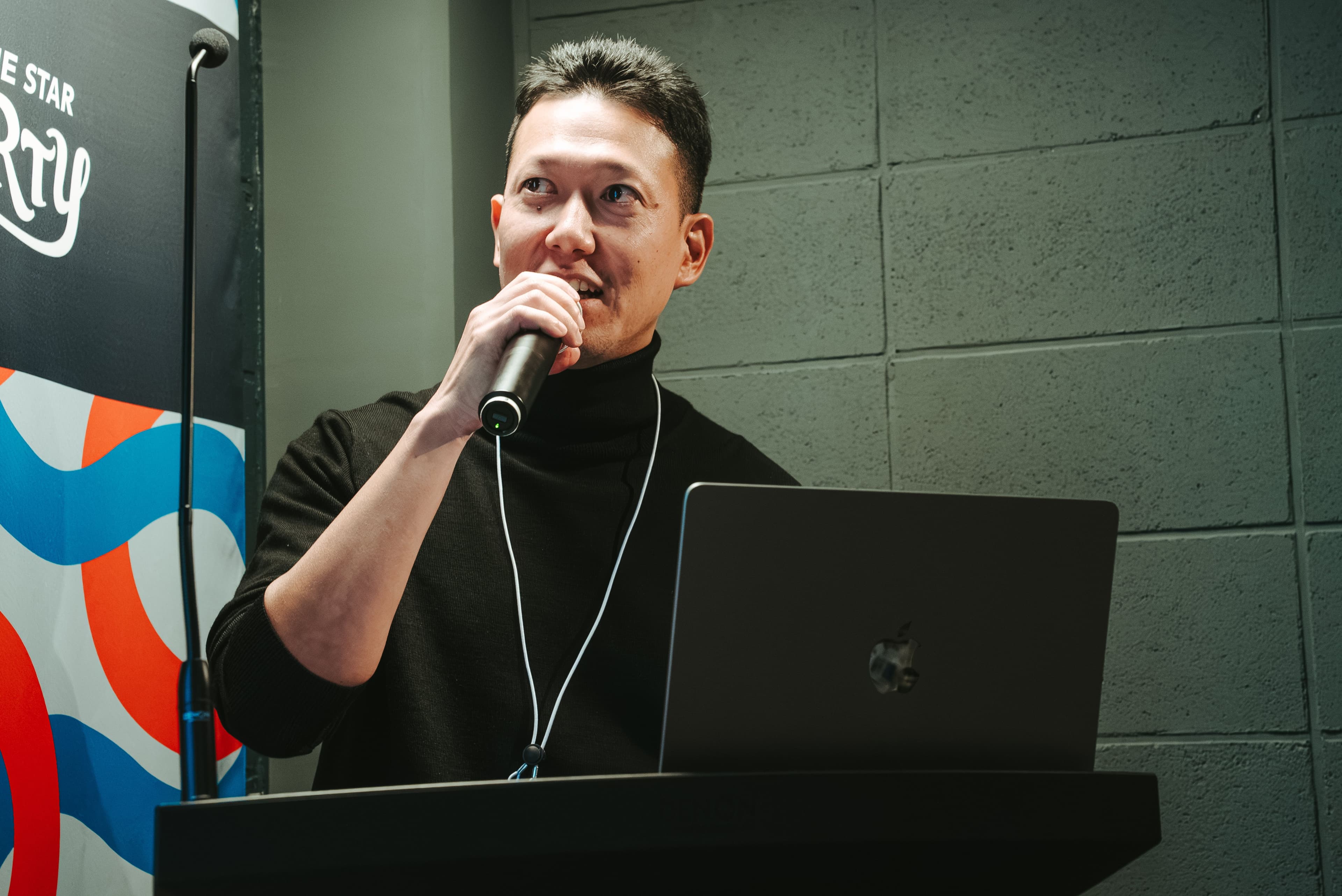 佐藤邦智がイベント会場の演台でマイクを持ち話している
